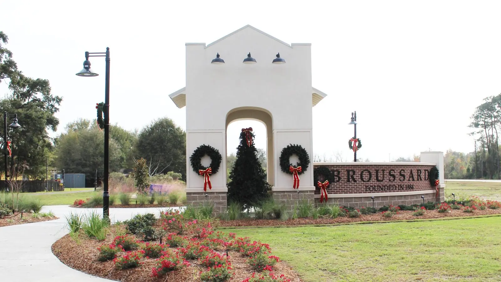 The City of Broussard entrance monument, a cream stucco arch with three lanterns beside a brick wall reading Broussard, founded in 1884
